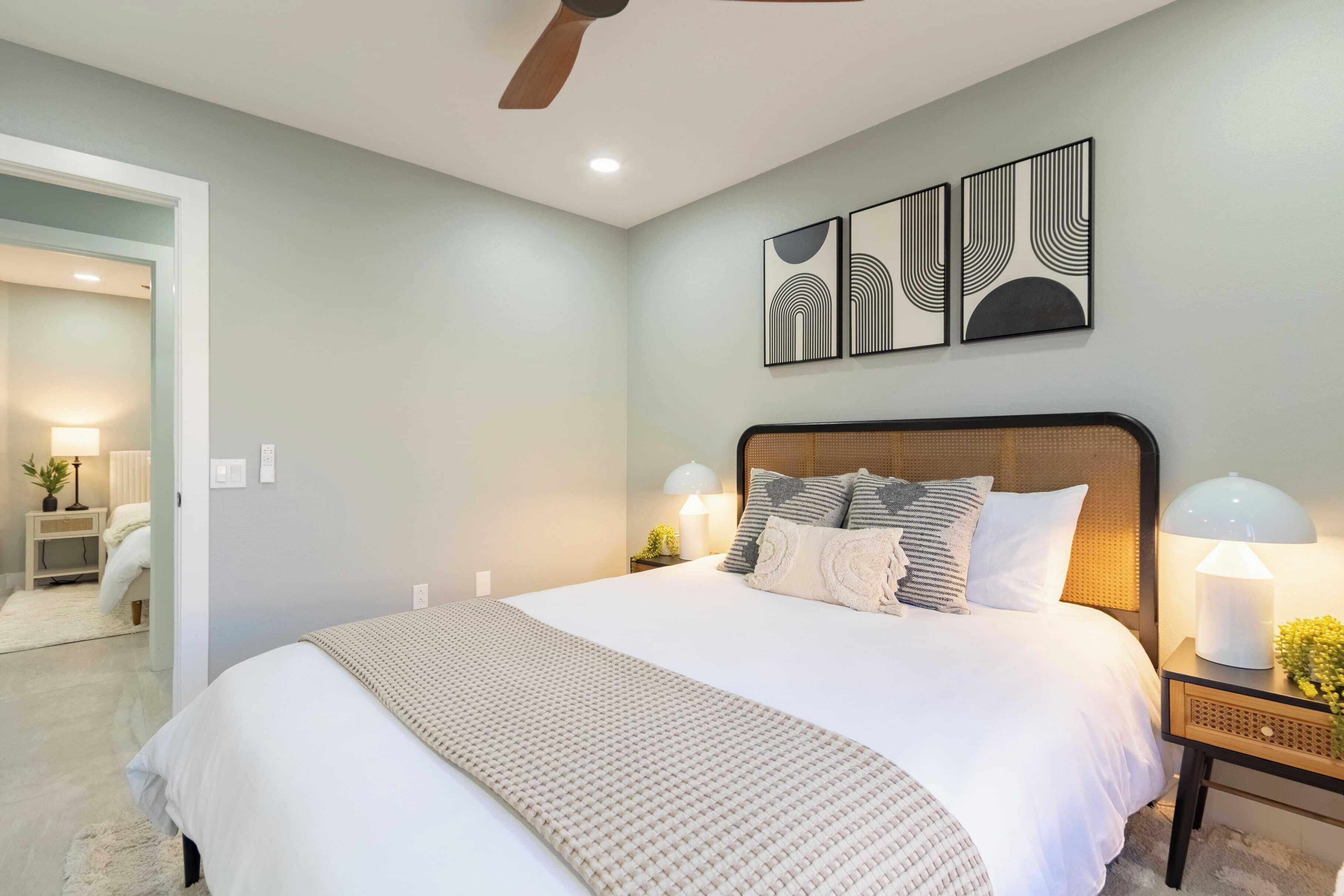 A bedroom with a large bed, two bedside lamps, and a ceiling fan.