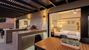 A modern hotel room with a large bed, a wooden table, and a built-in grill area. - Calypso by Avantstay Entertainers Paradise Pool, Hot Tub, Putting Green (Indio)