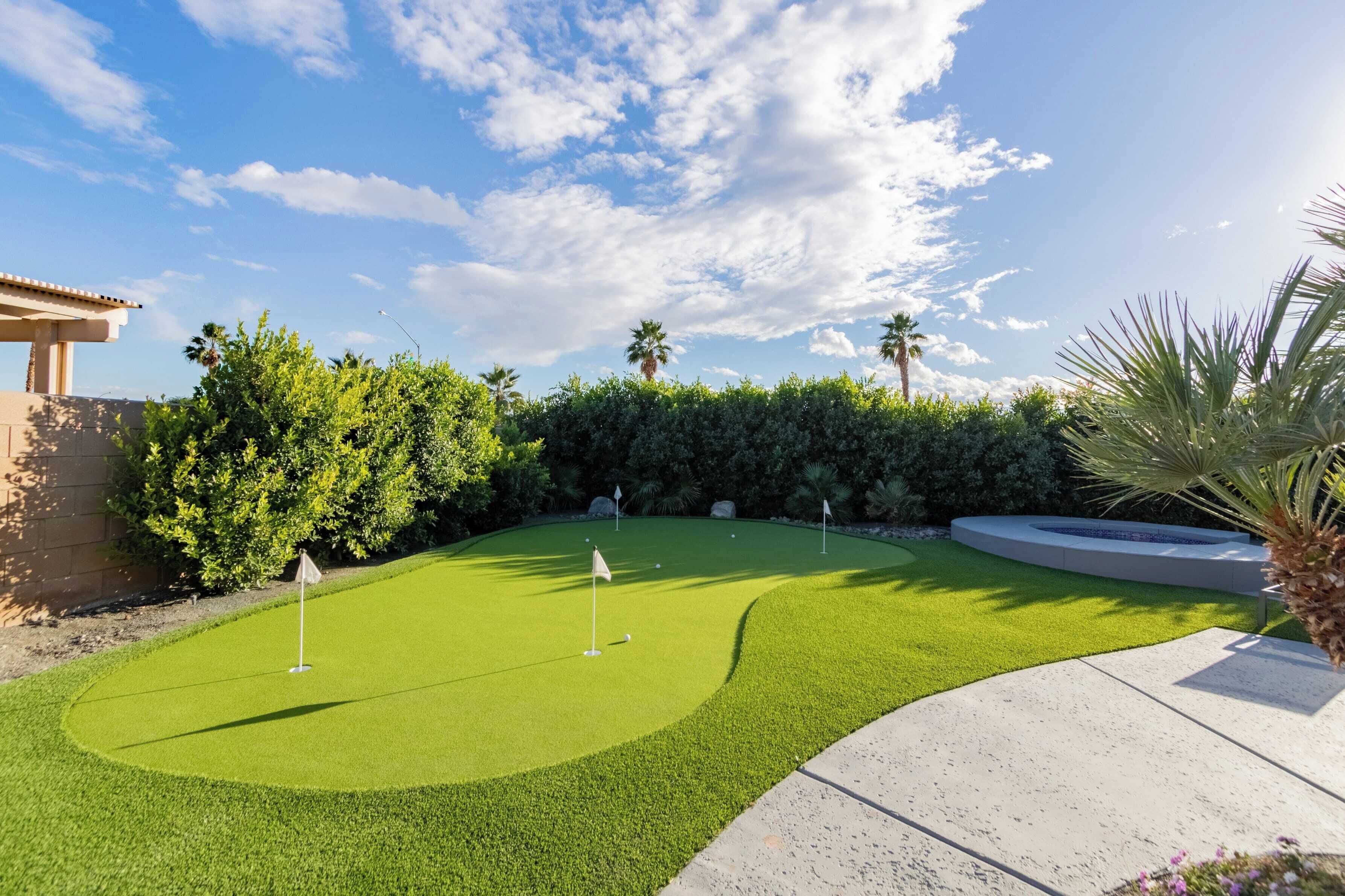 A well-maintained golf course with a clear sky, neatly trimmed hedges, and a palm tree.
