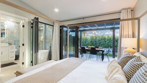 A modern bedroom with a large bed, a bathroom with a glass shower, and a dining area with a view of the outdoors. - Calypso by Avantstay Entertainers Paradise Pool, Hot Tub, Putting Green (Indio)