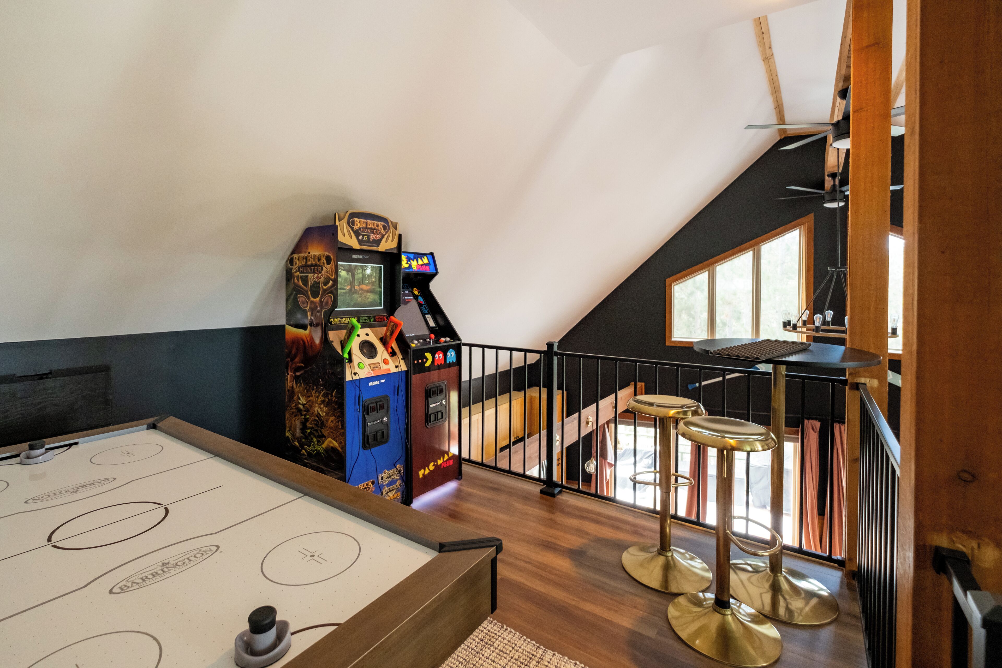 Ein Raum mit Billardtisch, zwei Spielautomaten, einem Barhocker und einer Treppe.