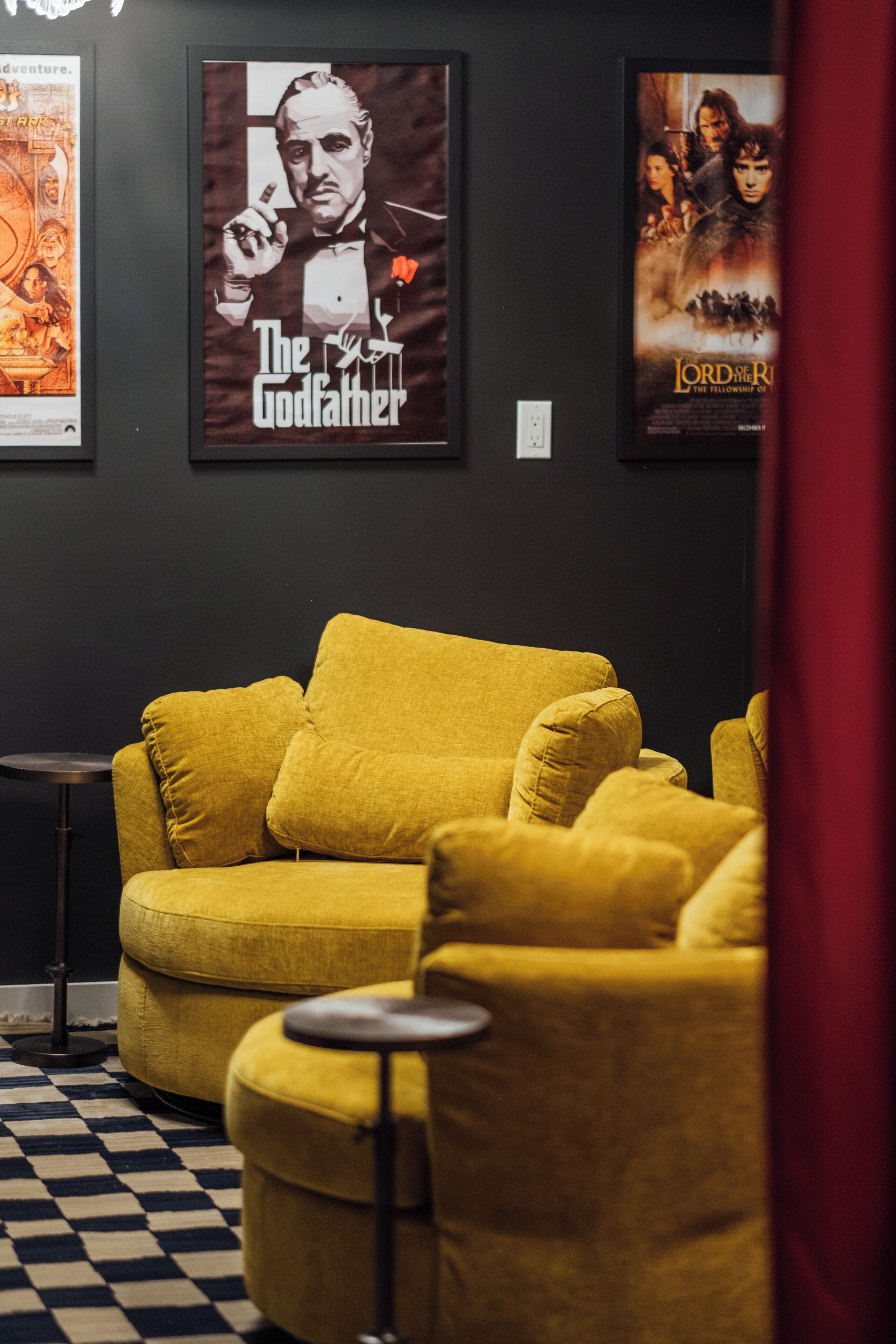 Una habitación con un sofá amarillo, una pequeña mesa redonda y carteles de películas en la pared.