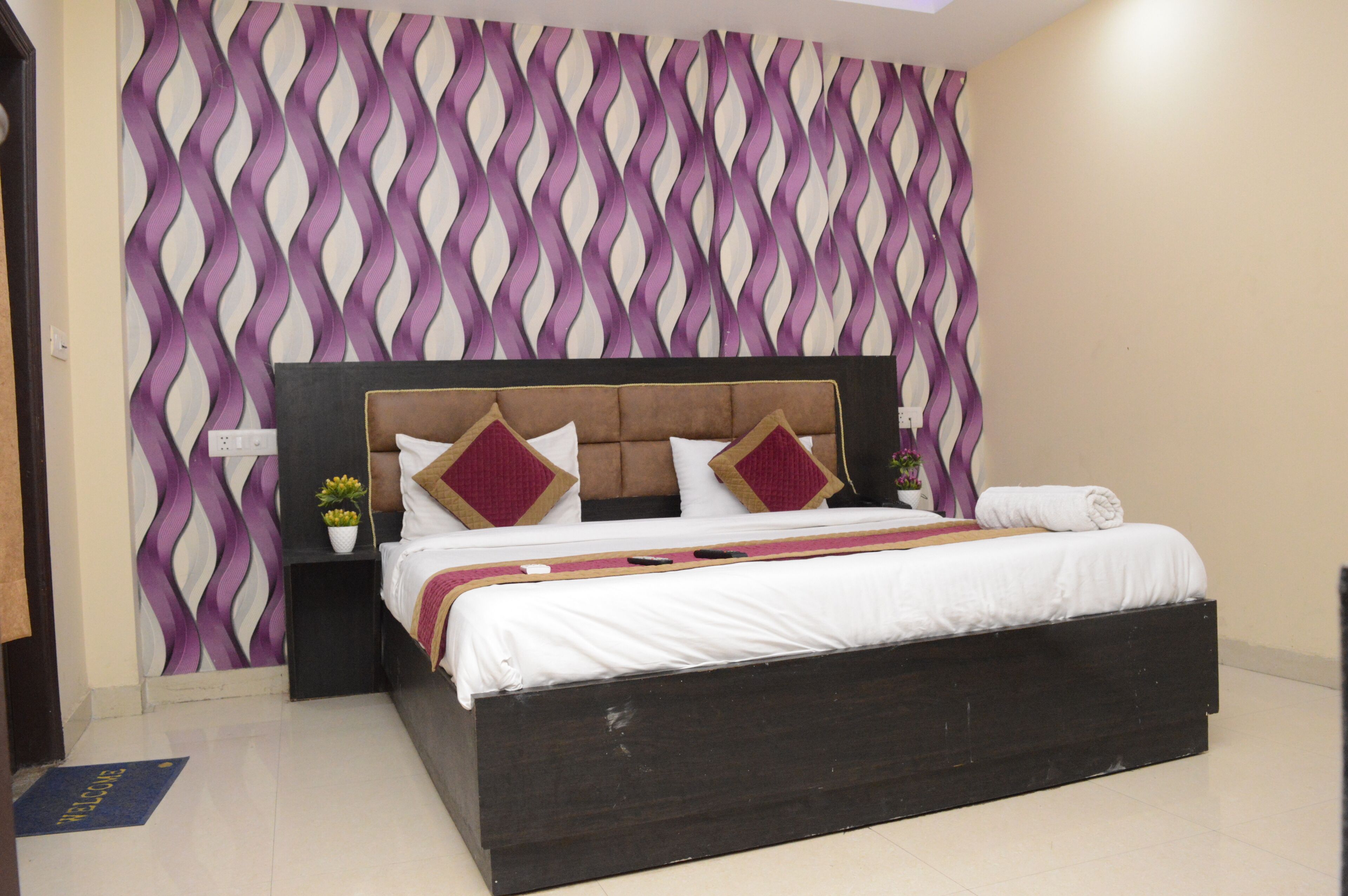 A bedroom with a bed, a headboard, a nightstand, a potted plant, and a decorative wall pattern.