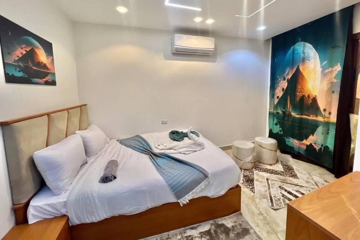 A modern bedroom with a bed, a wall-mounted air conditioner, and a large wall mural.