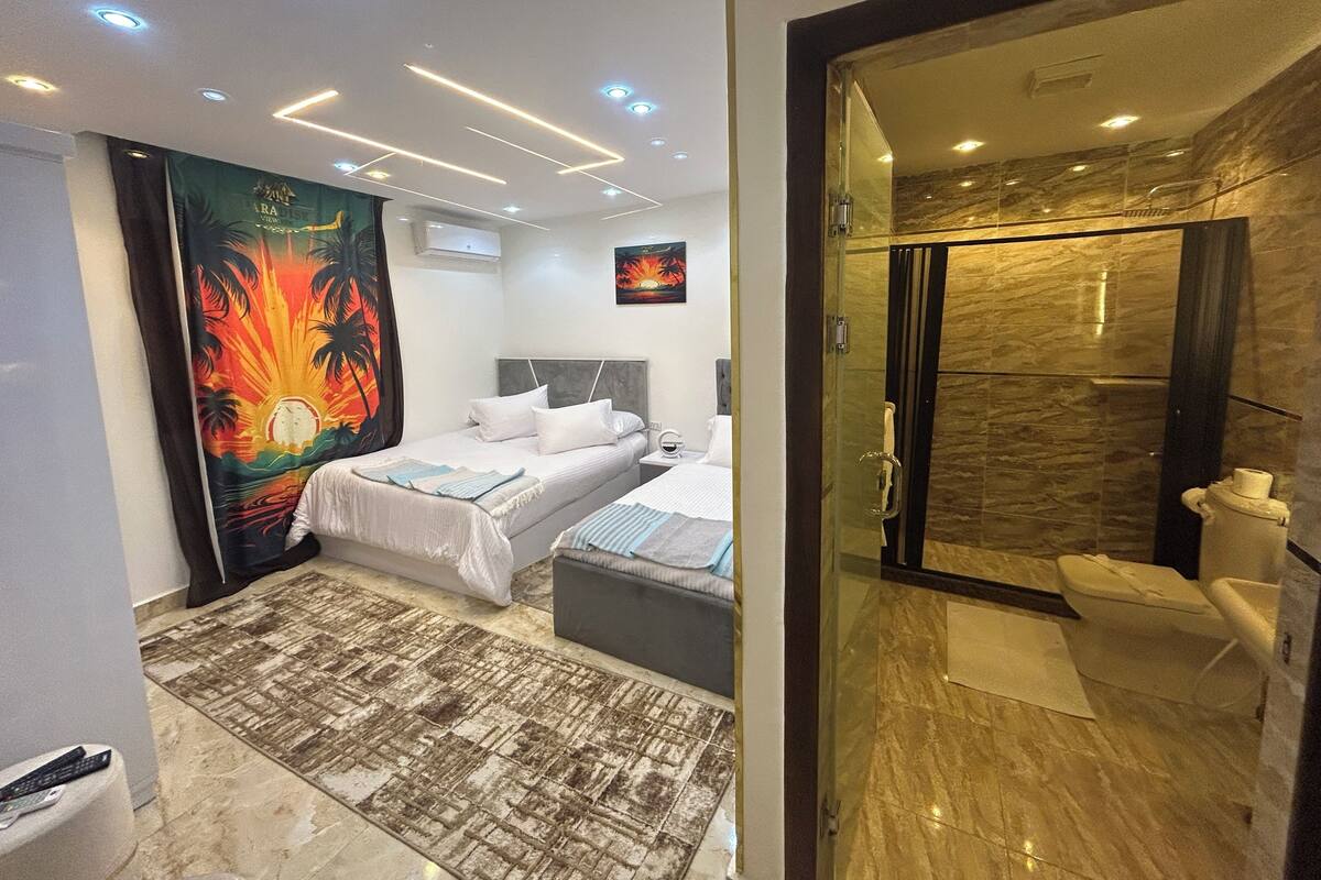 A modern hotel room with a bed, a bathroom with a glass shower, and a large curtain with a tropical design.