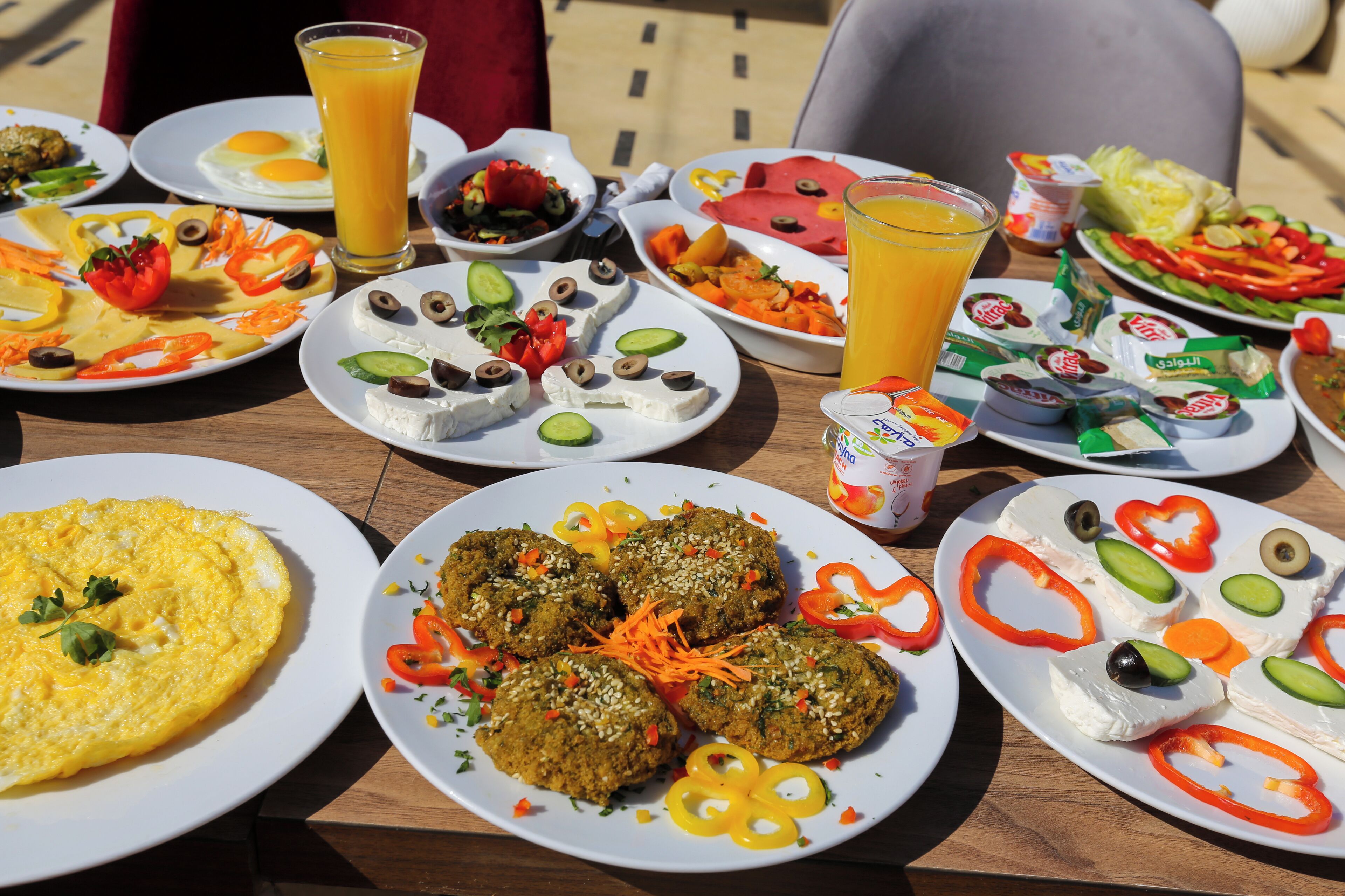A variety of breakfast dishes including eggs, omelets, and falafel, served on a wooden table outdoors.