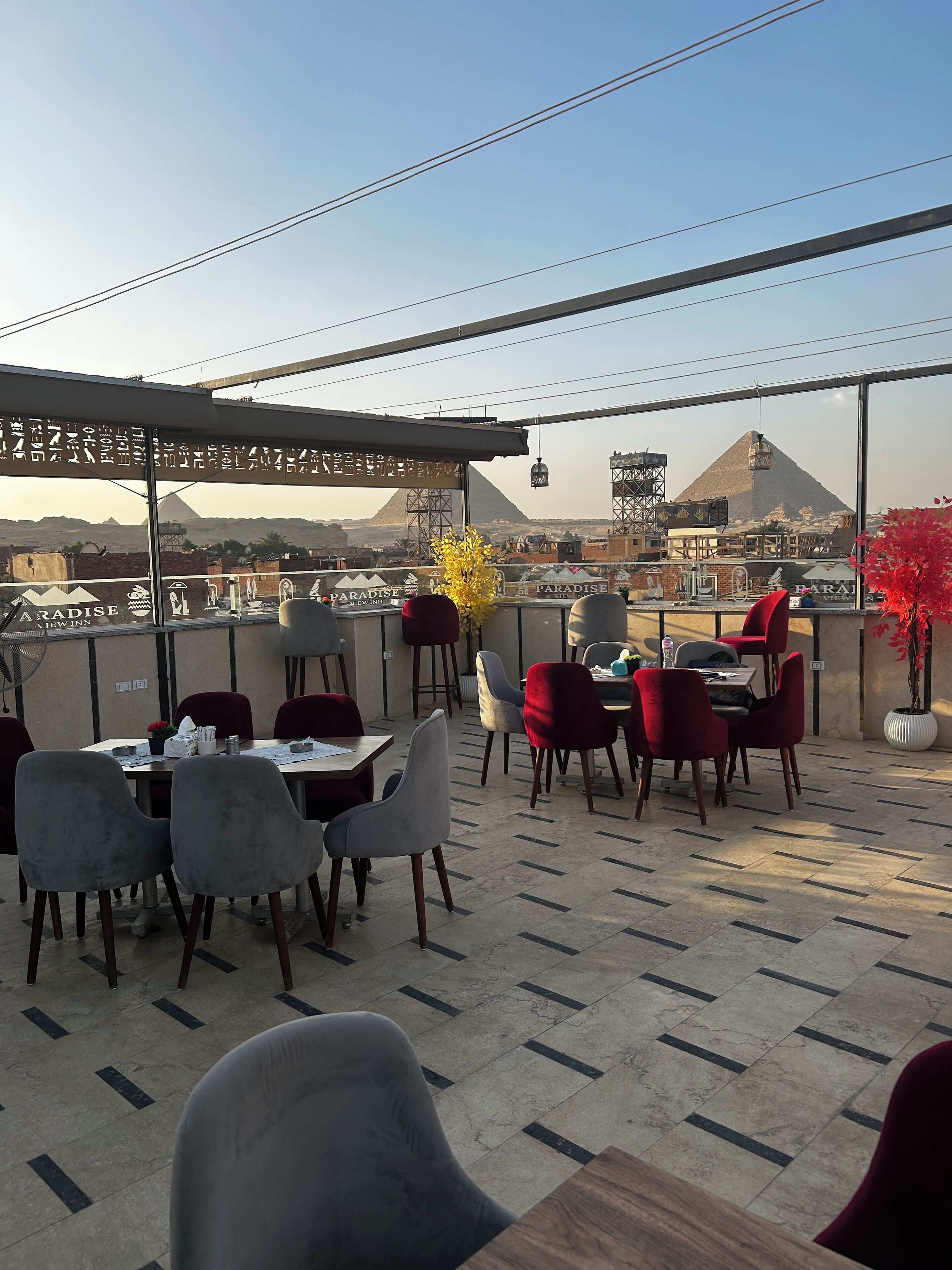 Un área de comedor al aire libre con mesas y sillas, vista a una pirámide y un letrero que indica Paradise View Inn.