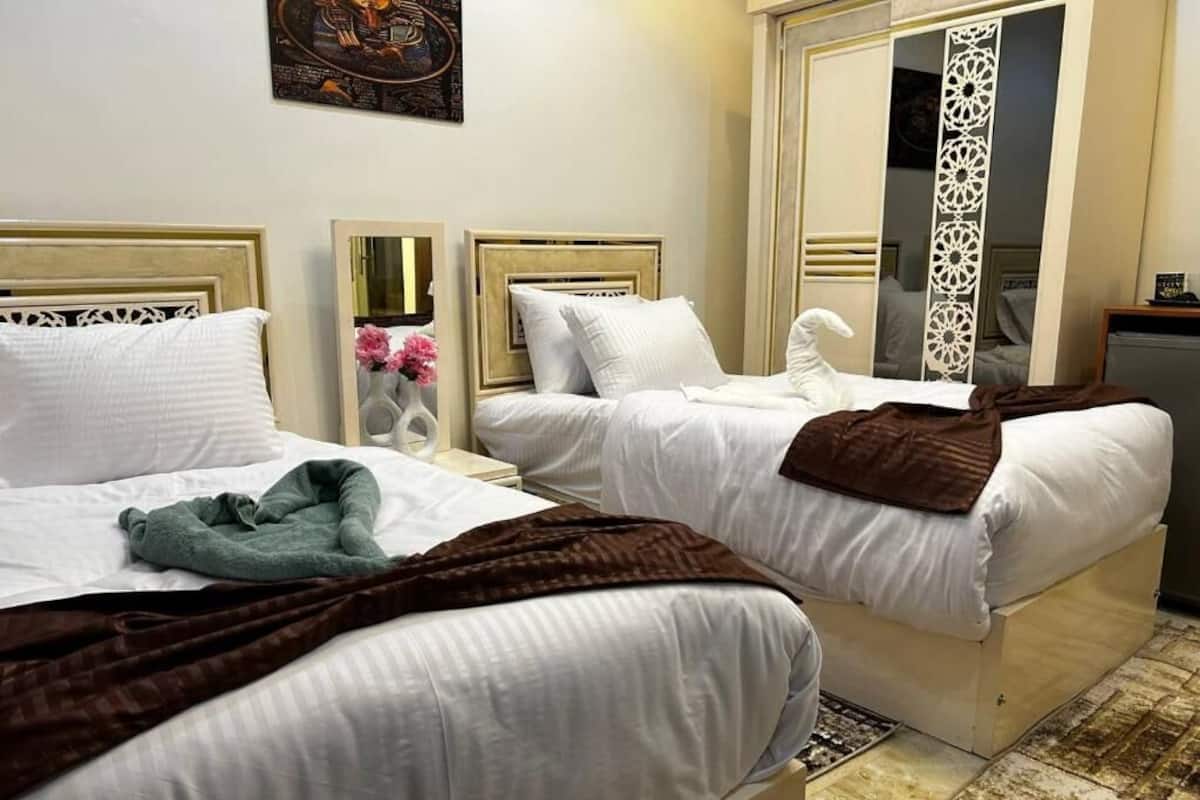 Two beds with white linens, a brown blanket on one, and a mirror on the nightstand.