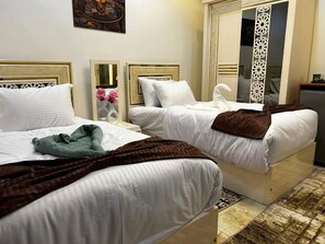 Two beds with white linens, a brown blanket on one, and a mirror on the nightstand. - Paradise Pyramids View INN  (Giza)