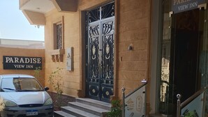A building with a sign reading "Paradise View Inn." There is a car parked in front, and the entrance has a black gate with decorative patterns. - Paradise Pyramids View INN  (Giza)