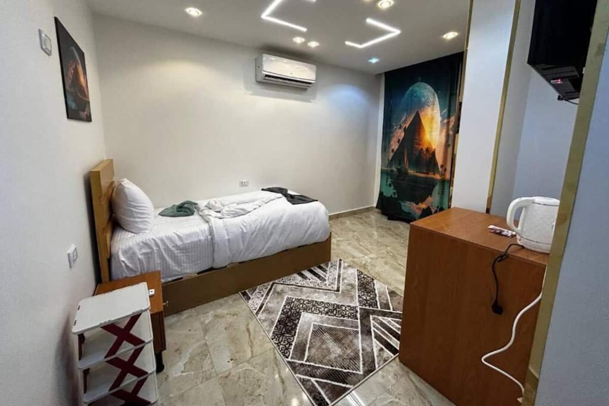A bedroom with a bed, a desk, an air conditioner, a wall-mounted TV, and a poster.