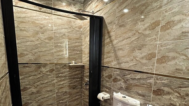 A modern bathroom with a walk-in shower, a toilet, and marble walls. - Paradise Pyramids View INN  (Giza)