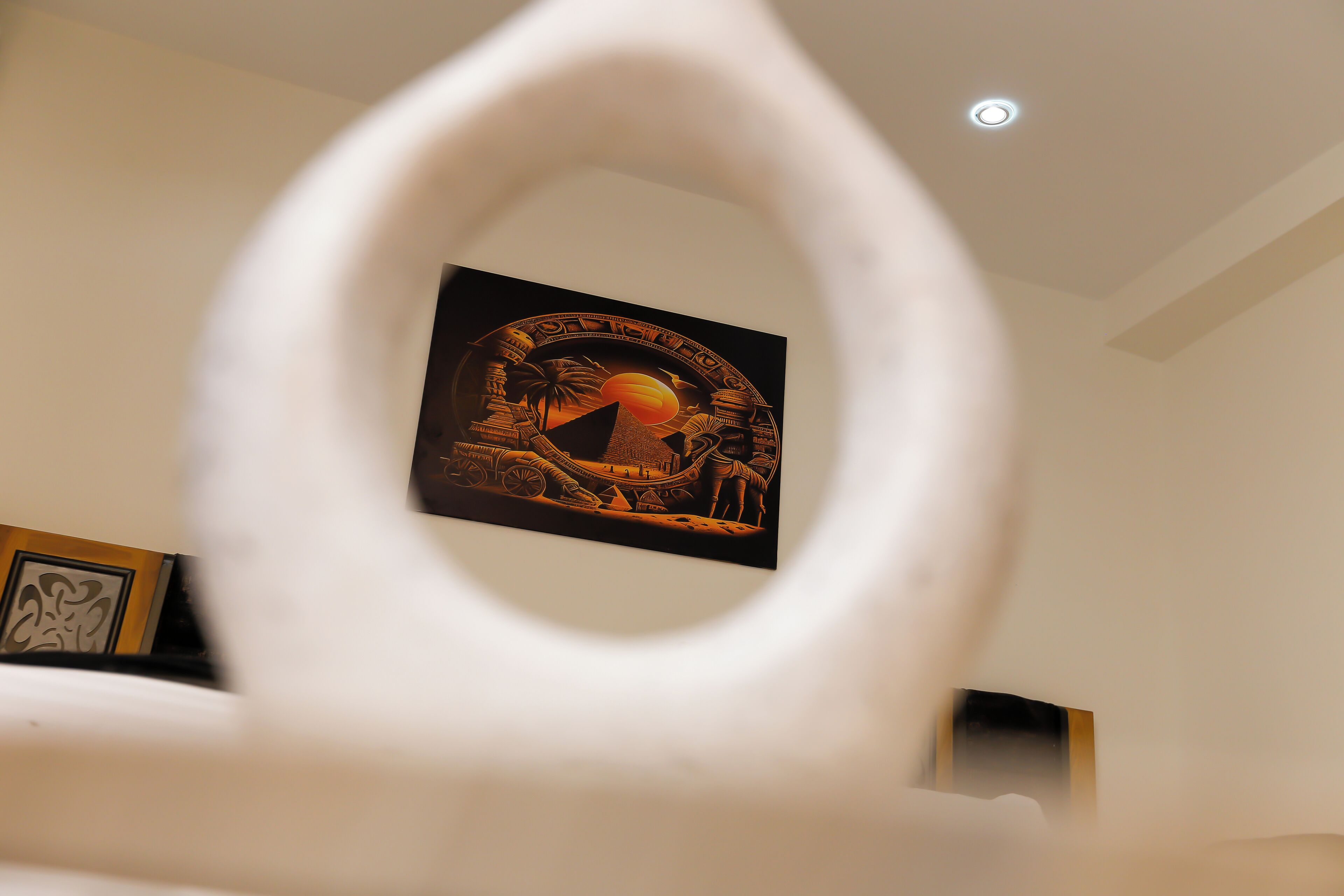Un'opera d'arte incorniciata su una parete, un oggetto circolare bianco in primo piano e una lampada a soffitto.