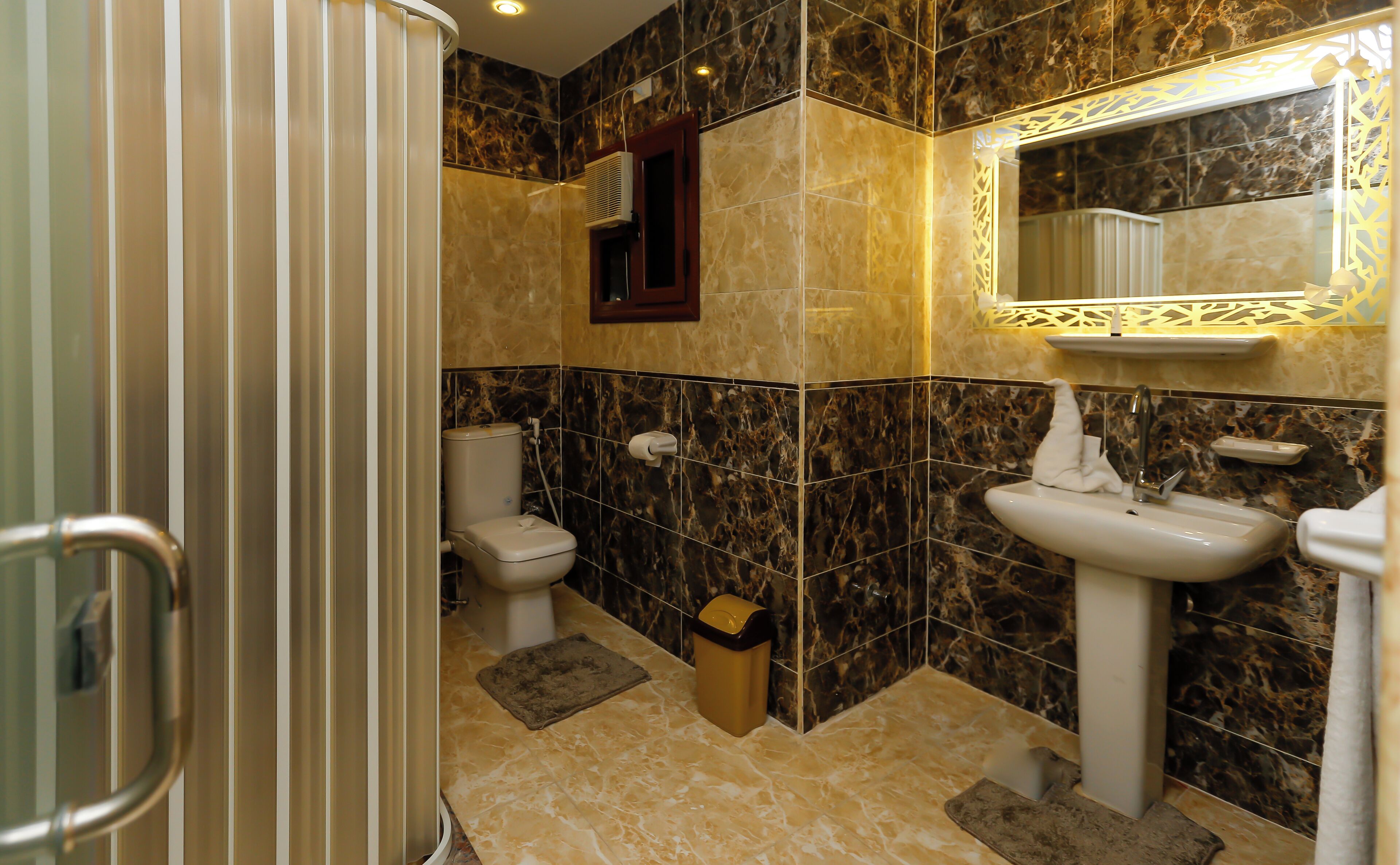 A bathroom with a toilet, sink, and shower. The walls are tiled with a marble pattern.