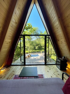 An attic room with a large glass window offering a view of a garden and outdoor seating area.