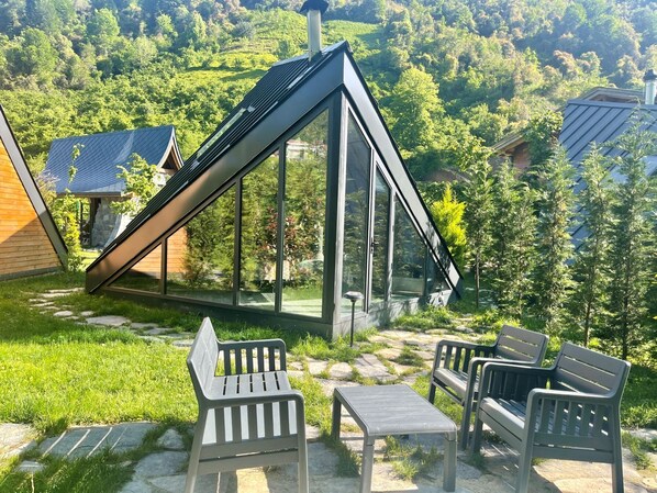 A modern house with a sloped roof and large windows, surrounded by a garden with benches and a small table. - DoğadaKal (Ardesen)