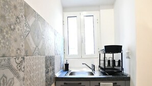 A compact kitchen with a window above the sink, patterned tiles on the walls, and a towel hanging on the cabinet door. - GreSi's home - Holiday home, in the heart of medieval Tivoli (Tivoli)