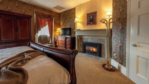 A bedroom with a large bed, a dresser, a TV, a fireplace, and a door. - MacVittie Room - Big Tree Inn

 (Geneseo)