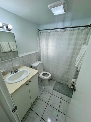 Un baño con lavamanos, inodoro y cortina de ducha blanca.