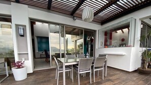 Ein offener Wohnbereich mit Glastür zum Balkon, einem Esstisch mit Stühlen und einer Küchenzeile mit Fenster.