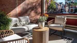 A balcony with wicker furniture, a potted plant, and a view of a town with red-roofed buildings. - Bethia Room - Big Tree Inn - In-Room Jacuzzi

 (Geneseo)