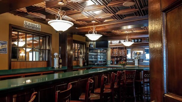 A bar area with a green counter, wooden chairs, and hanging light fixtures. - Bethia Room - Big Tree Inn - In-Room Jacuzzi

 (Geneseo)