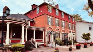 A red brick building with a white facade, a covered porch, and a flag. - Bethia Room - Big Tree Inn - In-Room Jacuzzi

 (Geneseo)