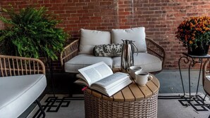 A cozy outdoor seating area with wicker furniture, a cushioned sofa, a coffee table, and a potted plant. - Bethia Room - Big Tree Inn - In-Room Jacuzzi

 (Geneseo)