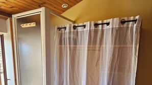 Une salle de bain avec un plancher en bois, un rideau de douche blanc et une porte en verre.
