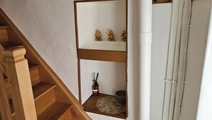 Un escalier en bois mène à un palier orné d’un mur blanc, d’un motif de feuille décorative au plafond et d’une étagère sur laquelle sont disposées de petites figurines.