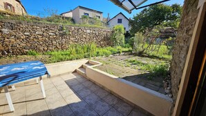 Un espace patio agrémenté d’un mur en pierre, d’une table bleue et d’un jardin où poussent différentes espèces de plantes.