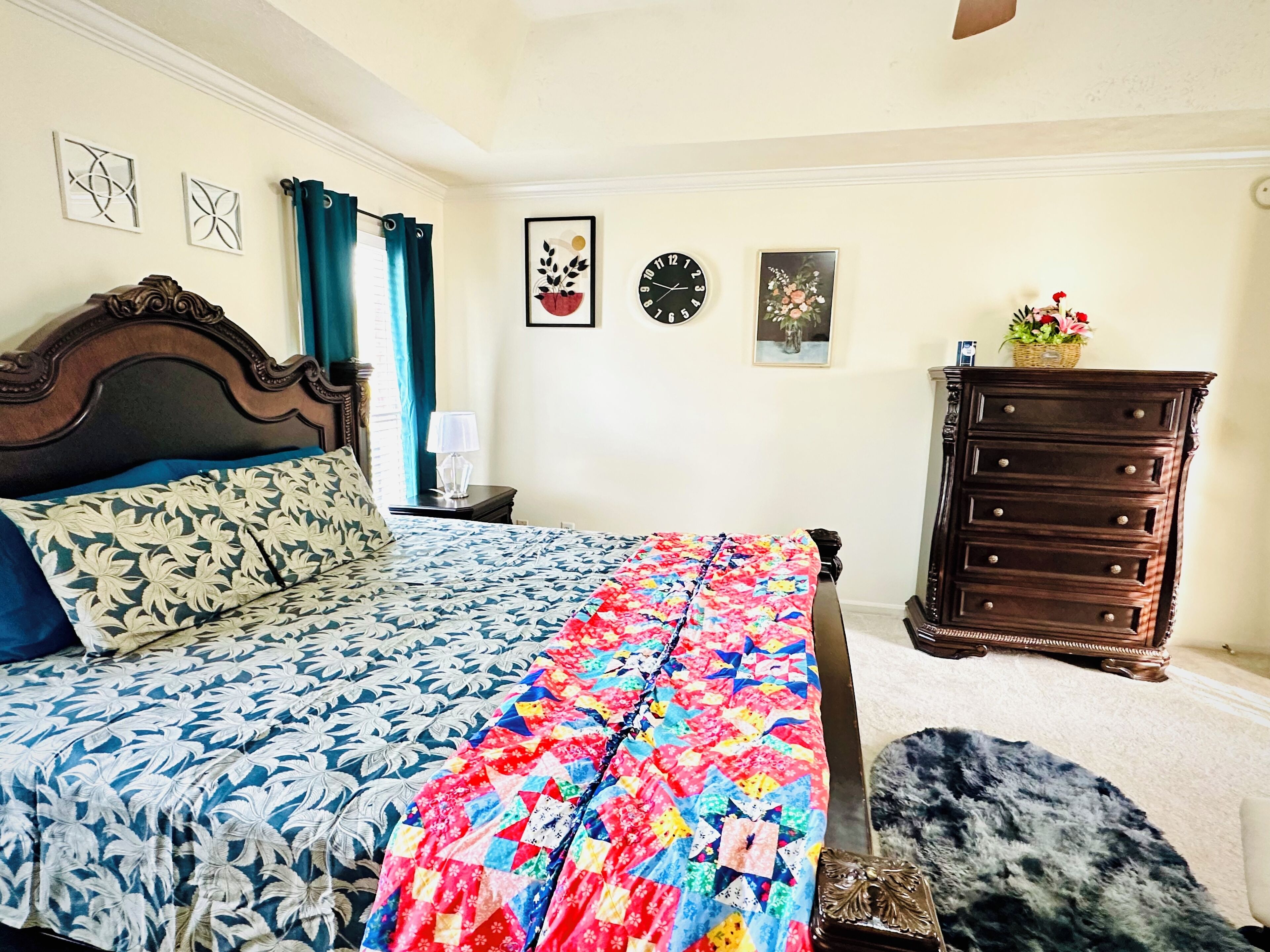 A bedroom with a bed, a dresser, a nightstand, a lamp, and decorative wall art.
