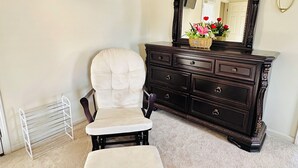 A room with a dark wooden dresser, a white upholstered chair, a small white bench, a wall-mounted TV, and a radiator. - Elegant Master Suite w/ Walk-in Closet & Private Entry in Prime Location MGM! (Montgomery)