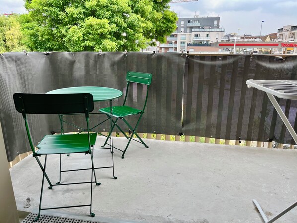Un espace patio extérieur avec une table verte et deux chaises vertes, un étendoir blanc et une grille métallique.
