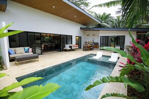 Una casa moderna con piscina, mobiliario de exterior y zona de cocina.