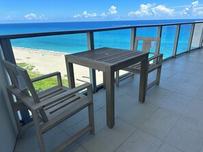 A balcony with a wooden table and two chairs, overlooking a beach and the ocean. - Spectacular Beach front with WiFi, fitness room and Spa service  (Riviera Beach)