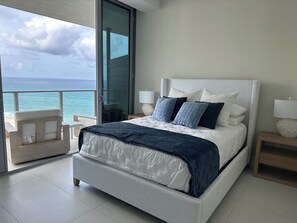 A bedroom with a large bed, two bedside tables, a chair, and a view of the ocean. - Spectacular Beach front with WiFi, fitness room and Spa service  (Riviera Beach)
