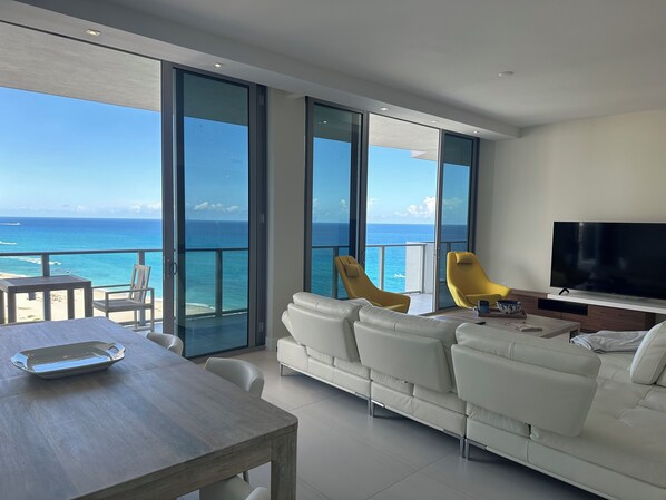 A modern living room with a large white sofa, yellow chairs, a wooden table, and a flat-screen TV. - Spectacular Beach front with WiFi, fitness room and Spa service  (Riviera Beach)