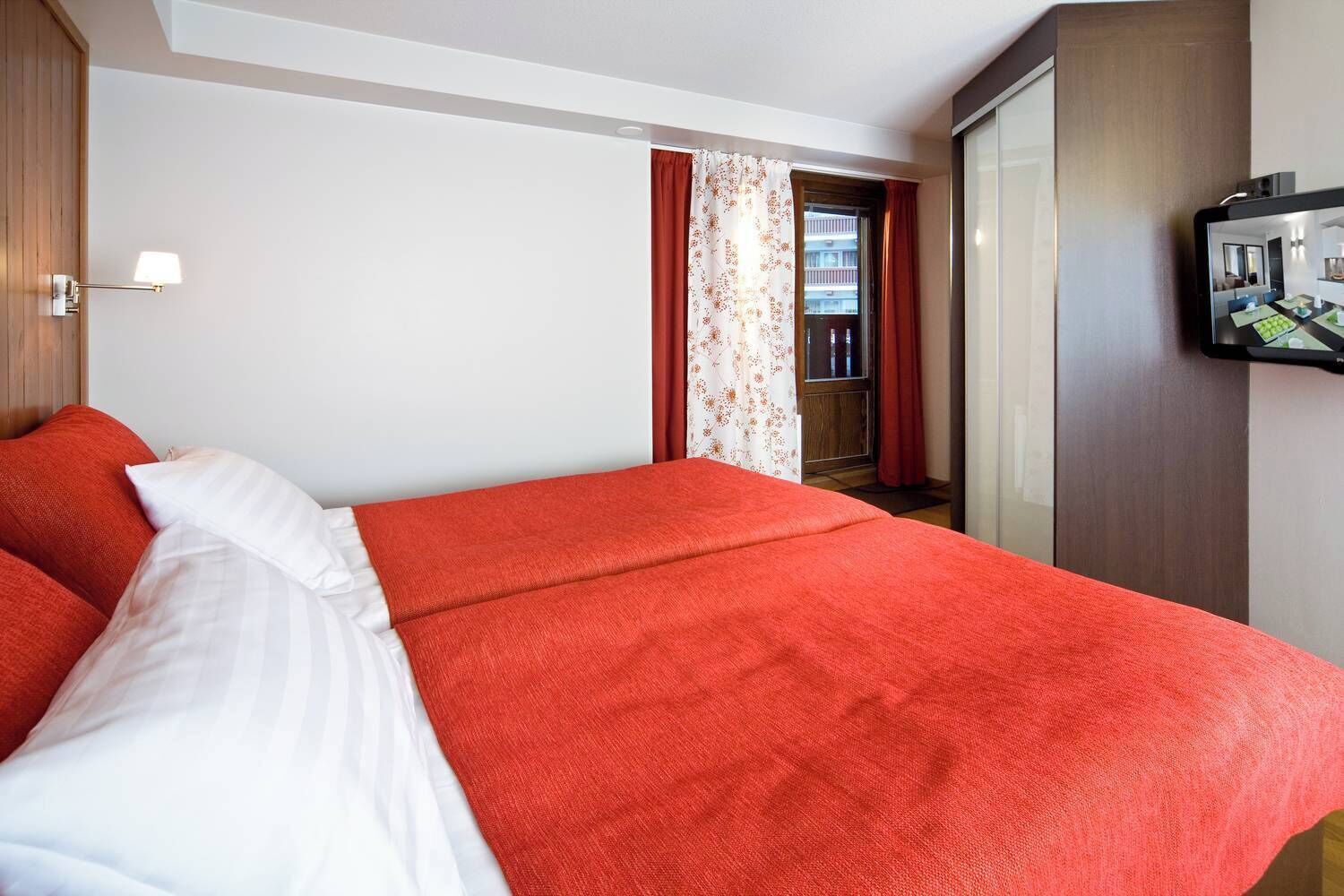 A hotel room with a bed, a TV, a wardrobe, and a window with curtains.
