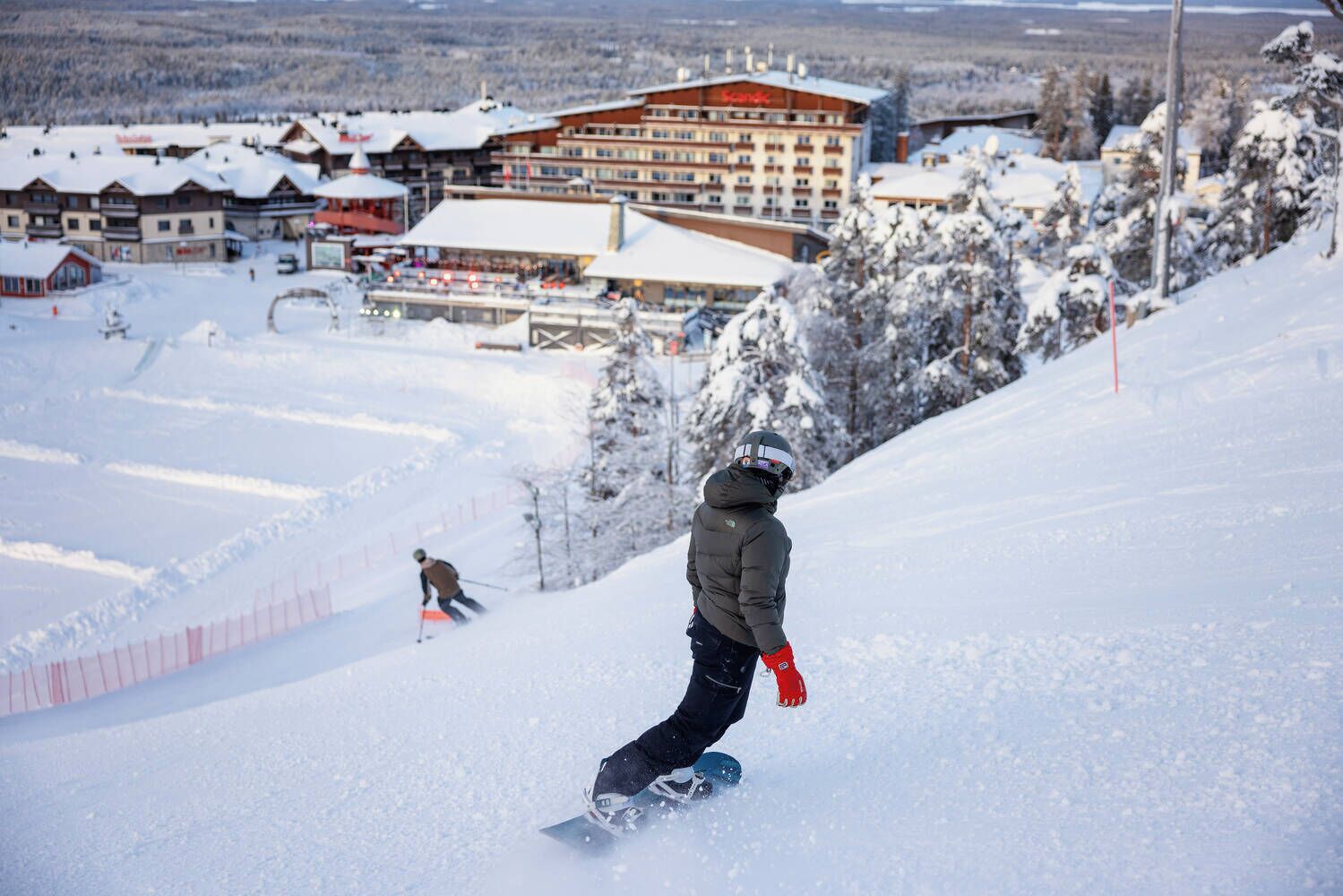 A snow-covered ski slope with a person snowboarding.