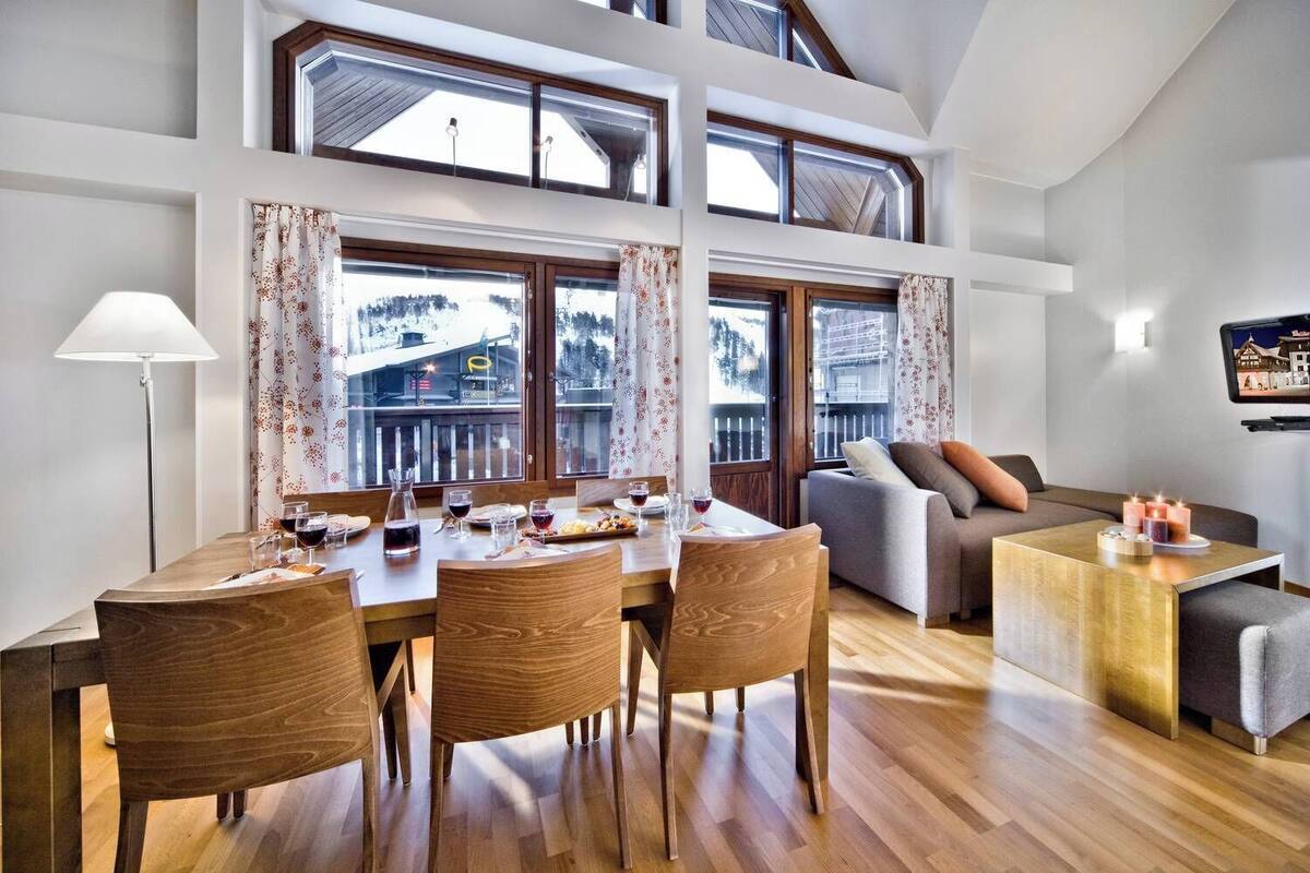 Un coin repas avec une table et des chaises en bois, un canapé et un téléviseur posé sur un meuble.