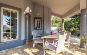A covered patio with a stone floor, a table with chairs, and potted plants. - Charming Villa Antonija (Novalja)