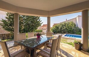 A covered patio with a glass table and wicker chairs, overlooking a swimming pool and greenery. - Charming Villa Antonija (Novalja)