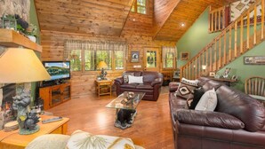 Un intérieur de chalet chaleureux avec un plafond en bois, des canapés en cuir, une cheminée et un téléviseur.