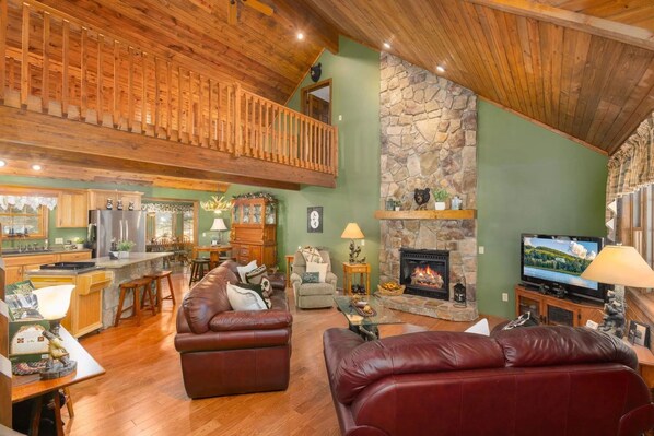 A spacious living area with a stone fireplace, wooden ceiling, and a cozy seating arrangement.