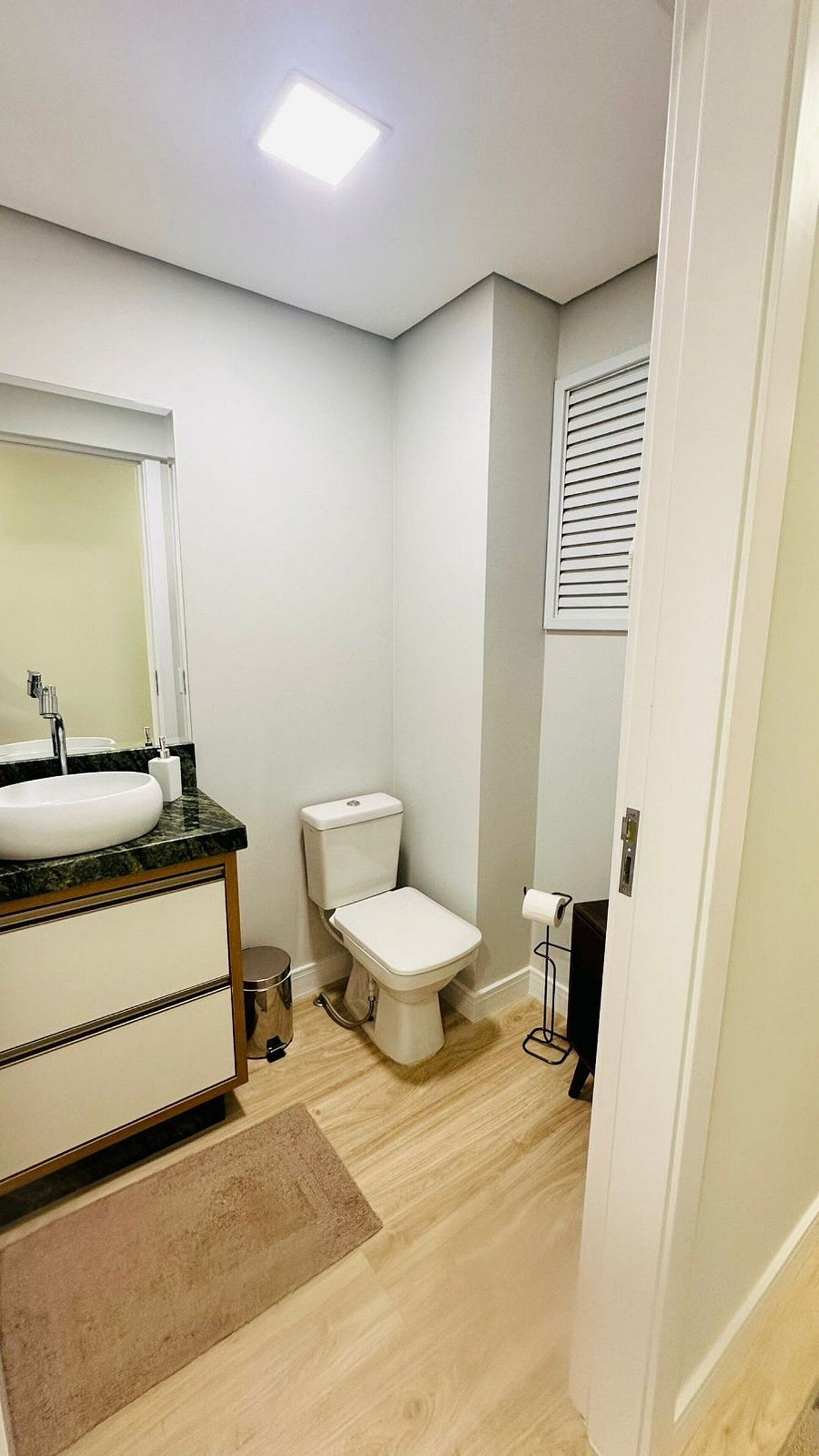 A bathroom with a white sink, mirror, toilet, and a small trash bin.