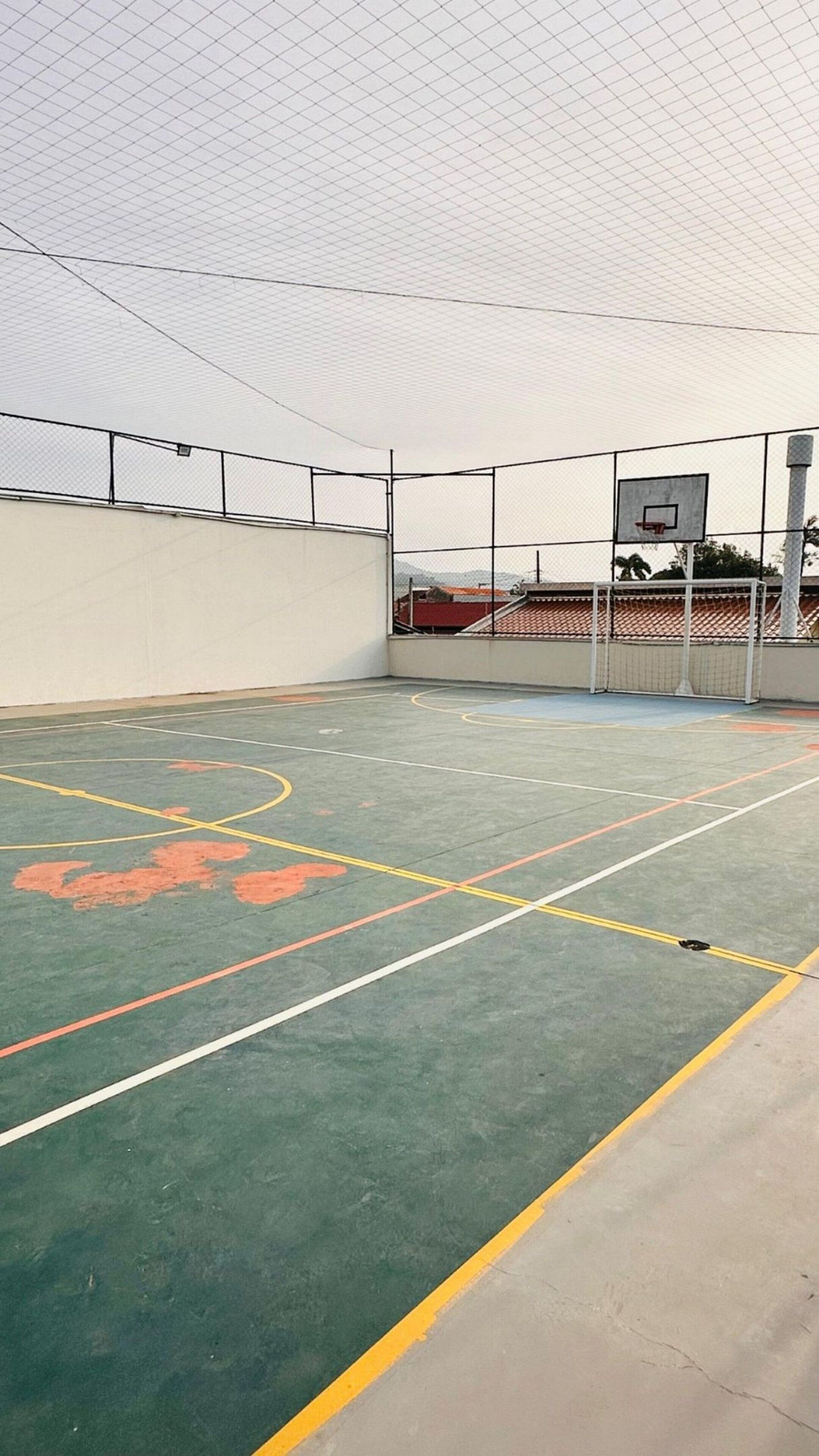 An indoor basketball court with a green playing surface, white and yellow lines marking the court, and a basketball hoop.