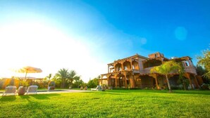 A large, two-story building with a traditional architectural style, surrounded by a well-maintained lawn and a few palm trees.