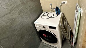 Un lavadero pequeño y moderno con lavadora y secadora LG de carga frontal, un tendedero metálico y un toallero de pared.