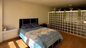 Un dormitorio con cama, mesita de noche, cómoda con plantas y ventana con persianas.